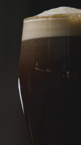 Vertikales-Video-Nahaufnahme-Von-Pint-Irish-Stout-Im-Glas-Vor-Schwarzem-Hintergrund-Zur-Feier-Des-1.-St.-Patricks-Day